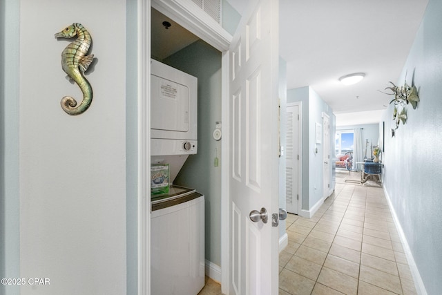 corridor featuring stacked washer and dryer, light tile patterned flooring, and baseboards