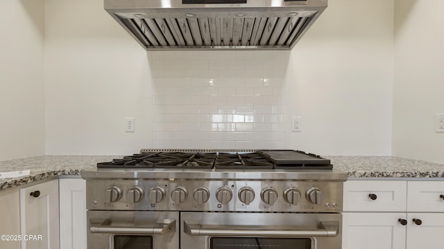 kitchen featuring light stone counters, range hood, tasteful backsplash, white cabinetry, and double oven range