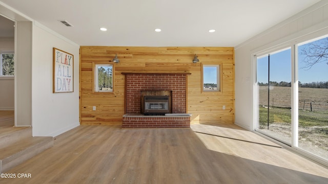 unfurnished living room with plenty of natural light, wooden walls, visible vents, and wood finished floors