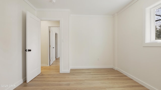 spare room featuring baseboards, light wood-style flooring, and crown molding