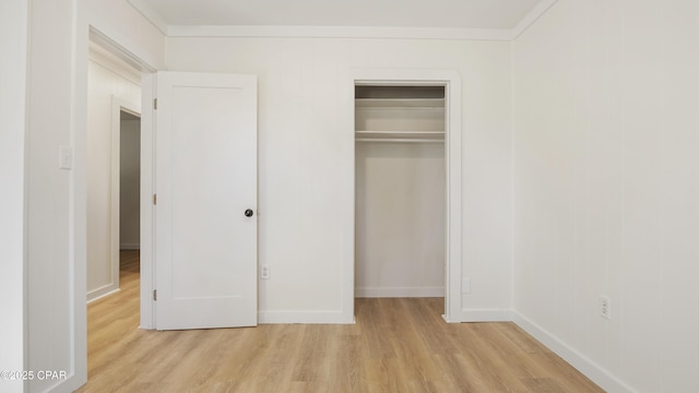 unfurnished bedroom with light wood-style floors, a closet, crown molding, and baseboards