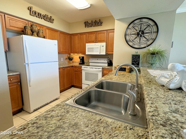 kitchen featuring white appliances, light tile patterned floors, brown cabinetry, and a sink