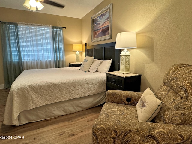 bedroom featuring a ceiling fan, a textured wall, and wood finished floors