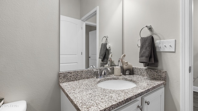 bathroom with vanity, toilet, and a textured wall