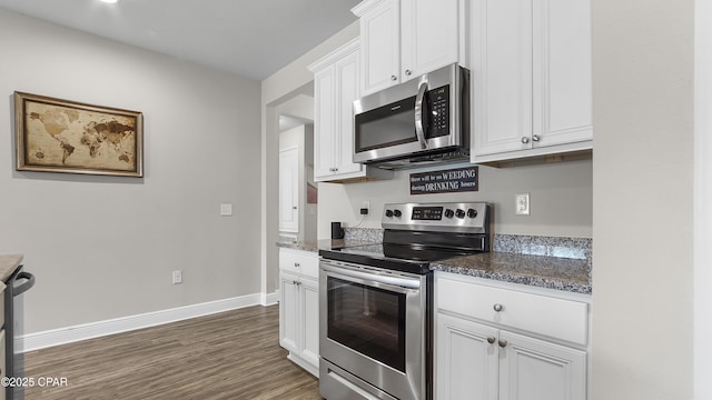 kitchen with wood finished floors, baseboards, dark stone counters, stainless steel appliances, and white cabinetry