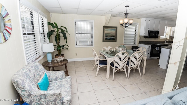 dining room with light tile patterned floors, baseboards, a paneled ceiling, and an inviting chandelier