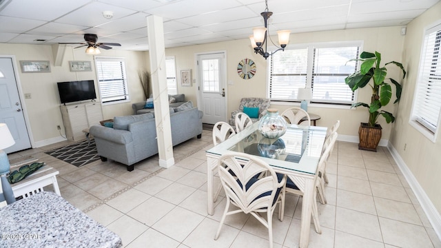 dining space with light tile patterned floors, ceiling fan with notable chandelier, baseboards, and a drop ceiling