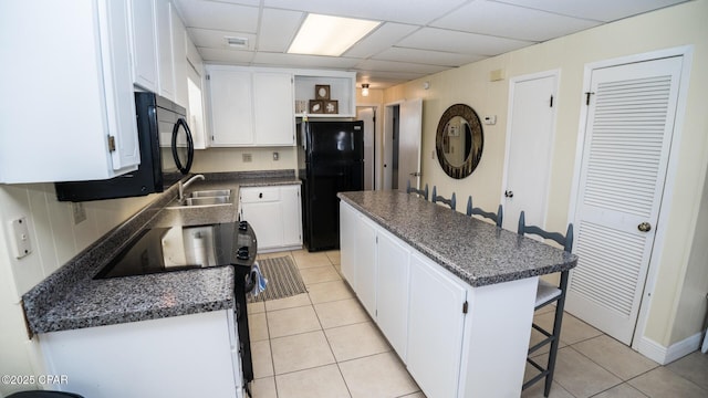 kitchen with dark countertops, a center island, a kitchen bar, black appliances, and a paneled ceiling