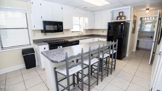 kitchen with light tile patterned floors, a paneled ceiling, black appliances, and white cabinetry