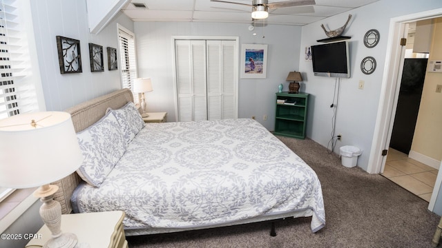 bedroom with tile patterned floors, a ceiling fan, a closet, carpet floors, and a paneled ceiling