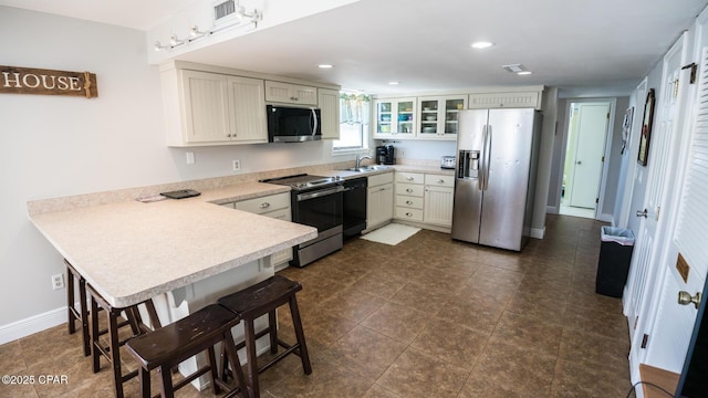 kitchen with a sink, appliances with stainless steel finishes, a breakfast bar area, a peninsula, and light countertops