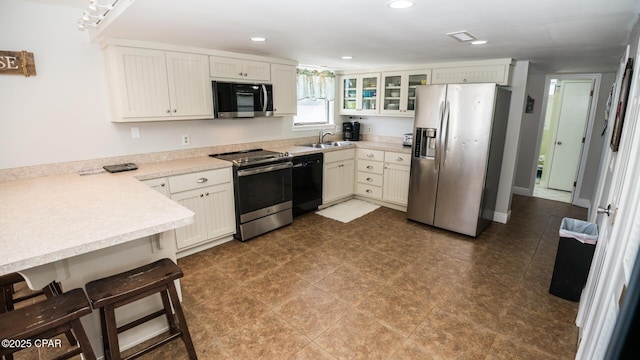 kitchen with a sink, recessed lighting, appliances with stainless steel finishes, light countertops, and glass insert cabinets