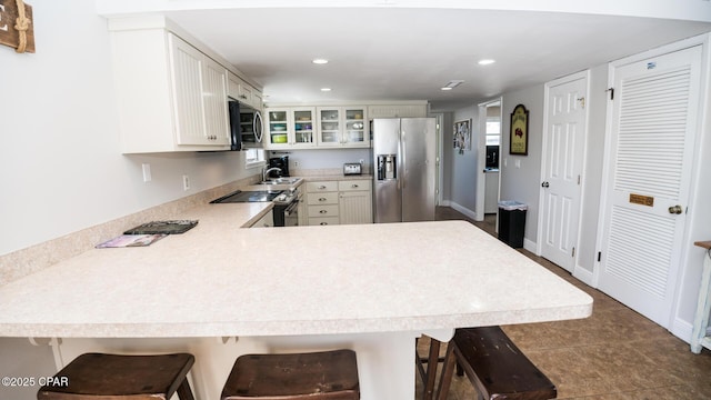 kitchen with a sink, stainless steel appliances, a peninsula, light countertops, and glass insert cabinets