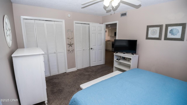 bedroom featuring visible vents, multiple closets, carpet floors, a textured ceiling, and a ceiling fan