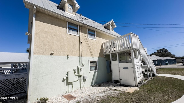 rear view of property with stucco siding, metal roof, and stairs