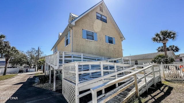 rear view of house with stucco siding, a wooden deck, driveway, and fence