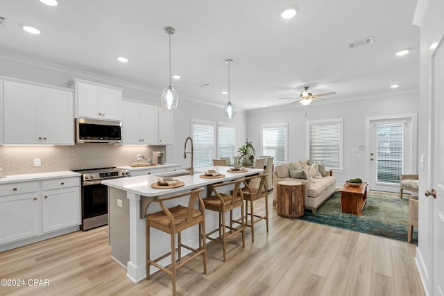 kitchen featuring light wood finished floors, stainless steel appliances, visible vents, ornamental molding, and a sink