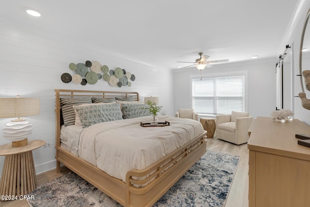 bedroom featuring light wood-type flooring, a barn door, and a ceiling fan