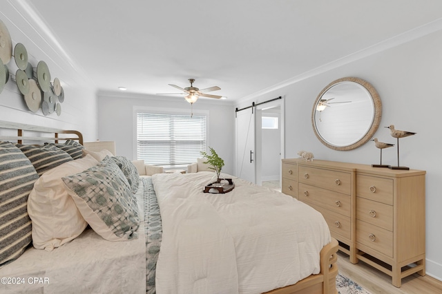 bedroom featuring light wood-style floors, crown molding, ceiling fan, and a barn door