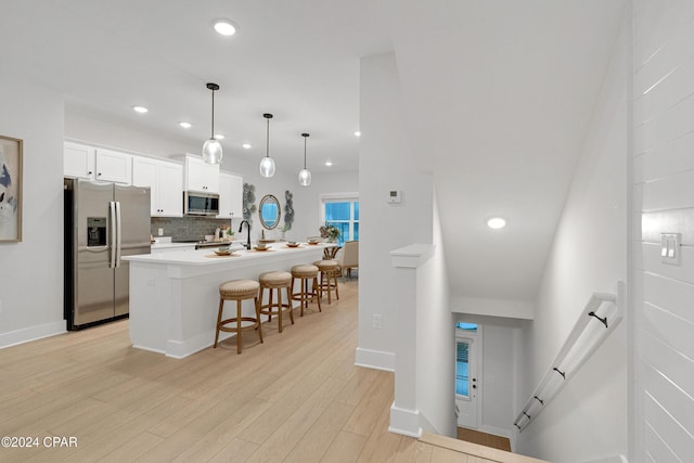 kitchen featuring decorative backsplash, a breakfast bar, stainless steel appliances, light wood-style floors, and white cabinetry