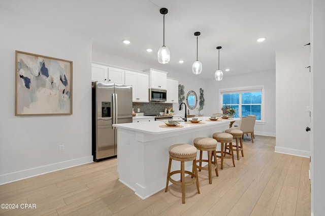 kitchen featuring a breakfast bar area, a kitchen island with sink, stainless steel appliances, light wood finished floors, and tasteful backsplash