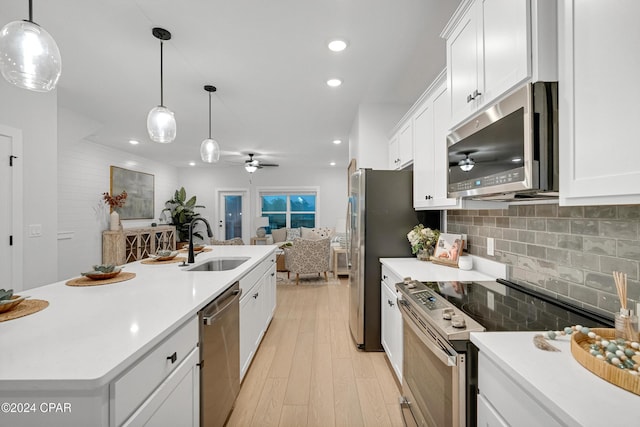 kitchen featuring ceiling fan, stainless steel appliances, a sink, white cabinets, and decorative backsplash