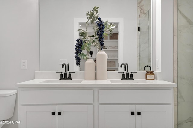 bathroom with a marble finish shower, a sink, toilet, and double vanity