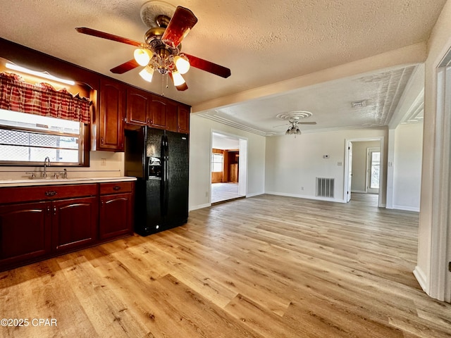 kitchen featuring a sink, black fridge, reddish brown cabinets, a textured ceiling, and light countertops