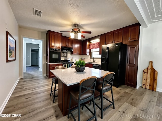 kitchen featuring a ceiling fan, under cabinet range hood, visible vents, a sink, and black appliances
