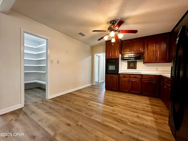 kitchen featuring a textured ceiling, under cabinet range hood, ceiling fan, visible vents, and black appliances