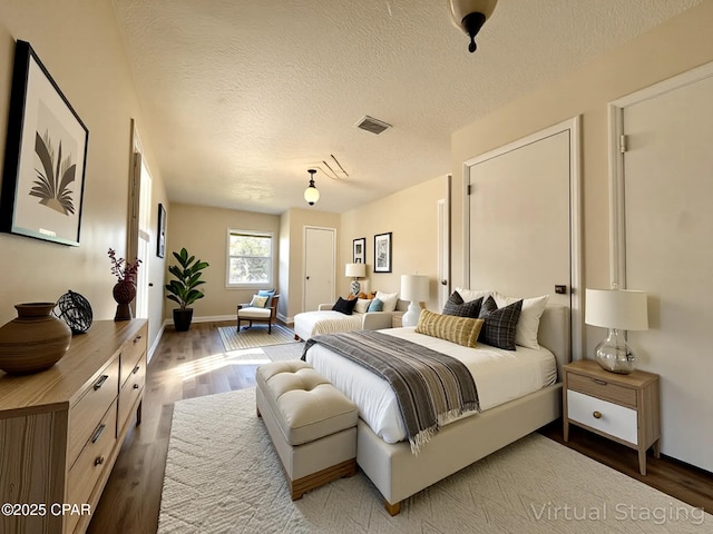 bedroom with baseboards, visible vents, a textured ceiling, and wood finished floors