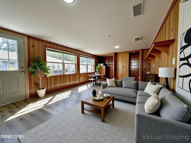 living area featuring light wood finished floors, wood walls, and visible vents