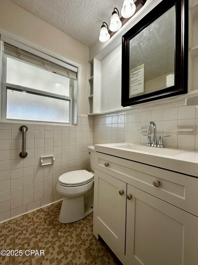 bathroom with tile walls, toilet, vanity, and a textured ceiling