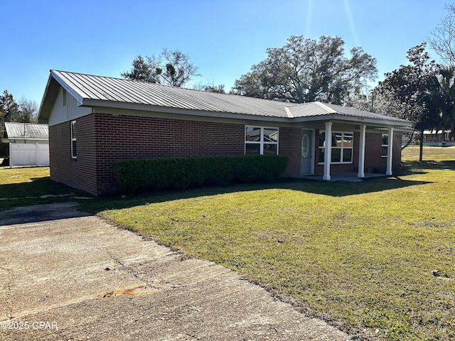 single story home featuring covered porch, a front yard, metal roof, and brick siding