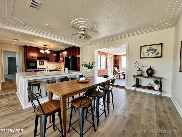 dining space with a textured ceiling, light wood-type flooring, visible vents, a ceiling fan, and baseboards
