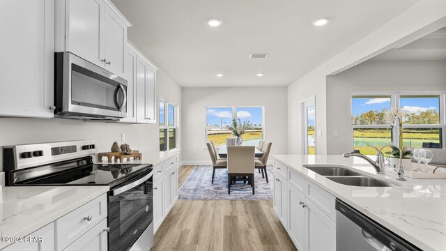 kitchen featuring light stone counters, appliances with stainless steel finishes, light wood-style floors, white cabinets, and a sink