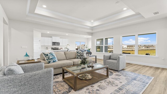 living room featuring a tray ceiling, light wood-type flooring, visible vents, and crown molding