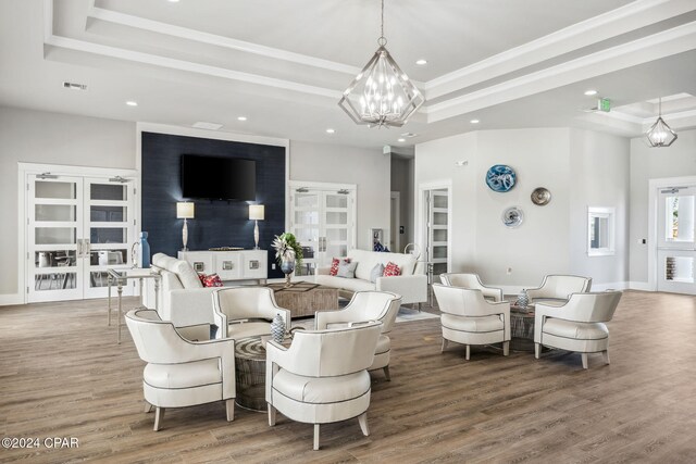 living area featuring a raised ceiling, a notable chandelier, french doors, and wood finished floors