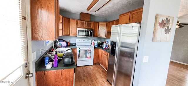 kitchen with light wood-type flooring, dark countertops, brown cabinets, stainless steel appliances, and a sink