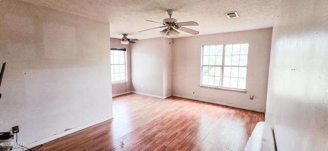 spare room featuring a textured ceiling, wood finished floors, visible vents, and a healthy amount of sunlight