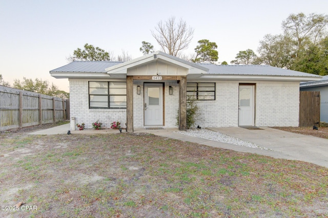 ranch-style home with metal roof, brick siding, and fence