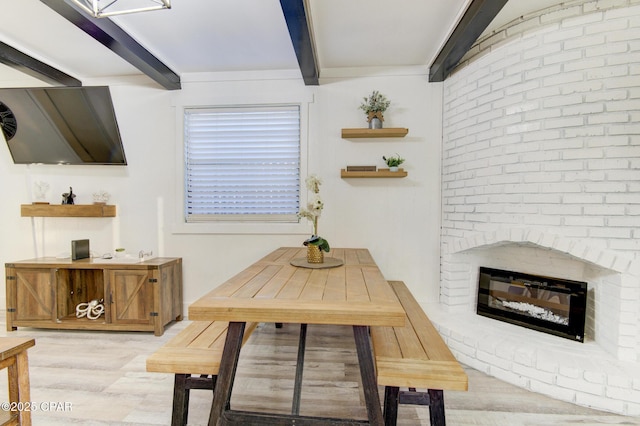 dining space featuring a brick fireplace, light wood-style flooring, and beam ceiling