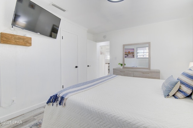 bedroom featuring baseboards, wood finished floors, visible vents, and crown molding