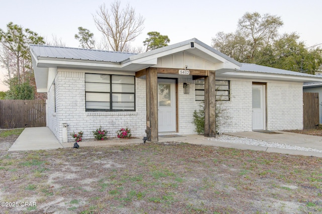 view of front of house with metal roof, brick siding, and fence