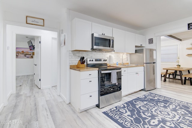 kitchen with tasteful backsplash, light wood-style flooring, appliances with stainless steel finishes, white cabinetry, and a sink