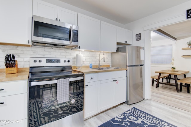 kitchen featuring stainless steel appliances, a sink, white cabinetry, light wood-style floors, and tasteful backsplash