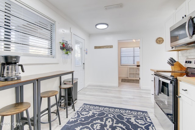 kitchen with light wood finished floors, backsplash, appliances with stainless steel finishes, white cabinetry, and baseboards