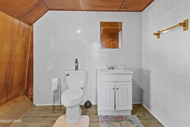 half bathroom featuring toilet, tile walls, wood finished floors, and vanity