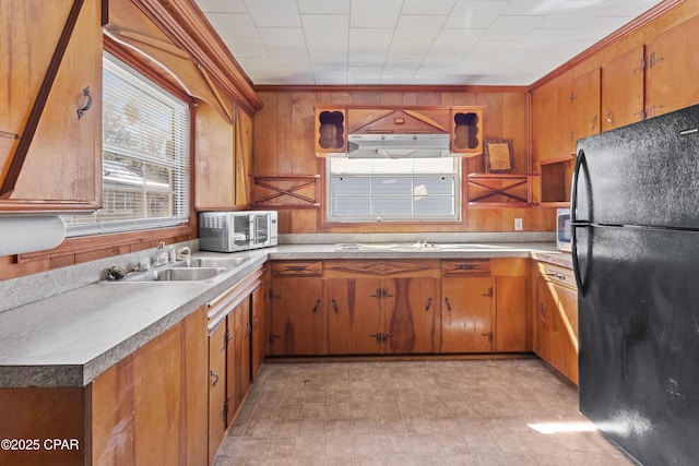 kitchen with stainless steel microwave, a sink, freestanding refrigerator, and brown cabinets