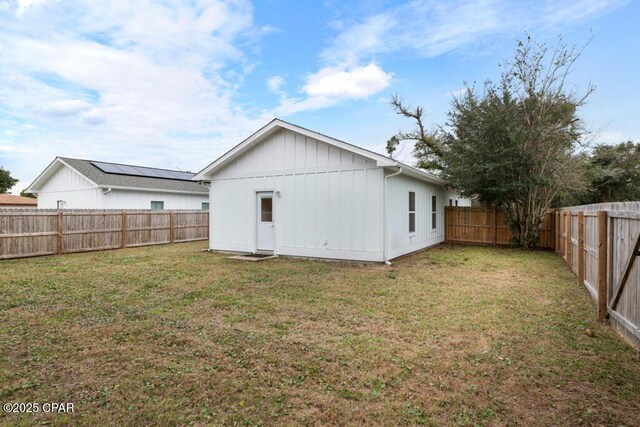 rear view of house with board and batten siding, a fenced backyard, and a yard